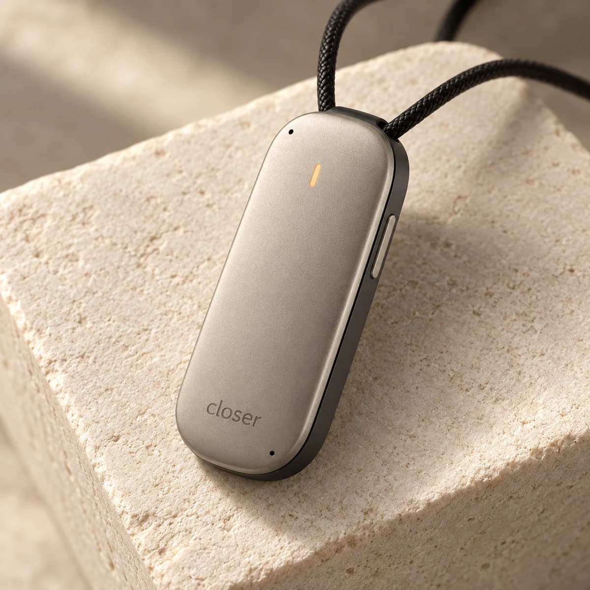 Photorealistic design study of the slim titanium-colored Closer pendant resting on warm stone, with its amber light and two microphone openings.